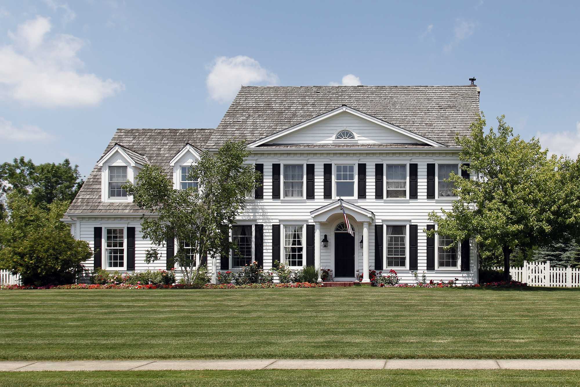 White colonial-style home with black shutters on a landscaped lot